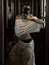 Person taking a mirror selfie wearing a white top and light-colored pants.
